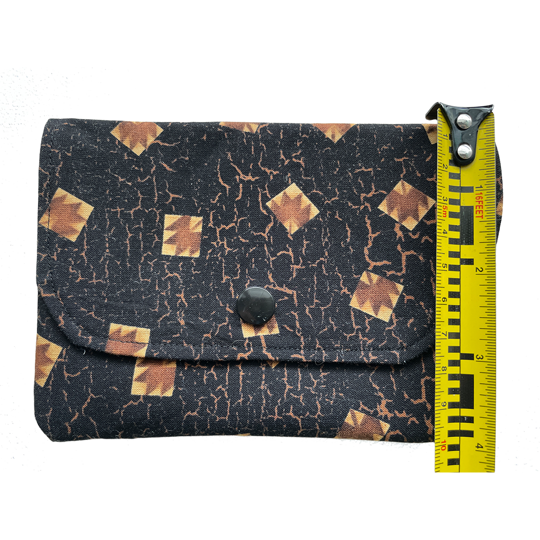 Black fabric pouch with gold geometric pattern next to a measuring tape on a white background